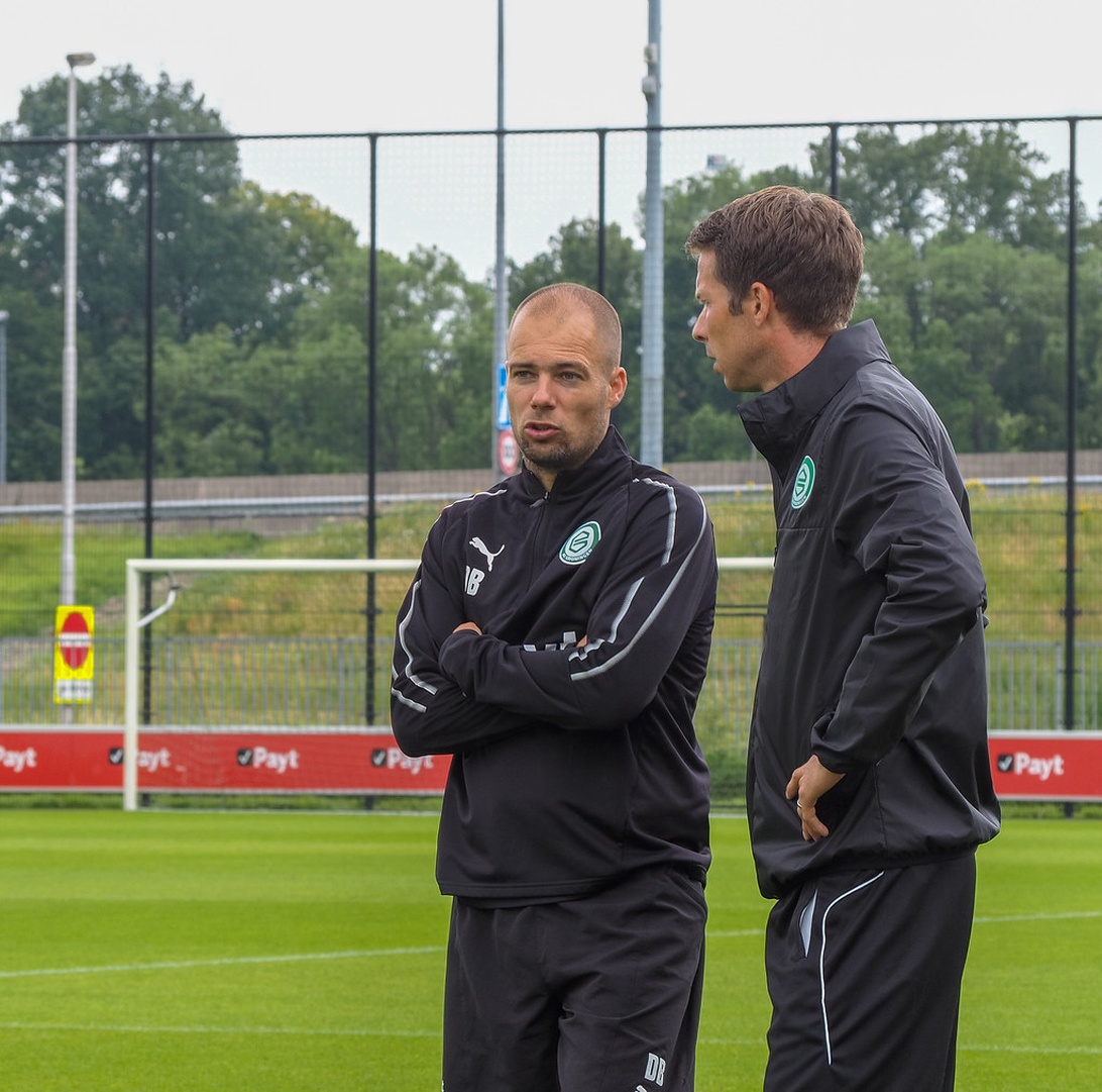 Två fotbollstränare i svarta Puma-träningsjackor på en träningsanläggning.
